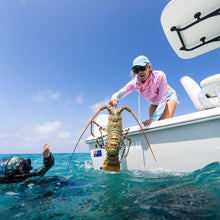 Load image into Gallery viewer, Person on a boat releasing a large lobster into the ocean with another person assisting.
