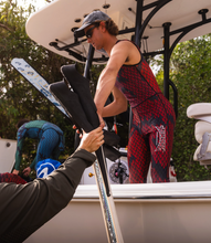 Load image into Gallery viewer, diver in Aimrite red/purple stinger suit passing dive fins out of boat
