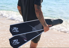 Load image into Gallery viewer, Person holding black diving fins with a logo on a beach
