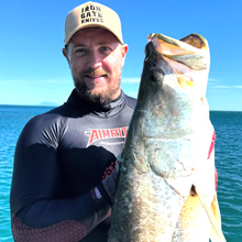 Load image into Gallery viewer, Diver holding barra in aimrite black stinger suit with clear blue sky
