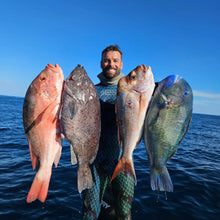 Load image into Gallery viewer, man holding fish on ocean in blue wetsuit
