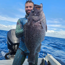 Load image into Gallery viewer, Man in wetsuit holding a large fish on a boat with blue ocean and sky in the background
